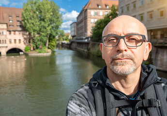 Nuremberg, Germany, August 3, 2023. Portrait of a middle-aged man with a view of the Hospital of the Holy Spirit on the Pegnitz River. Cityscape. Travel destinations.