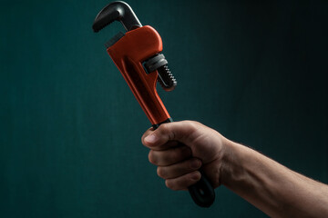 Adjustable pipe wrench in male hand on dark green background.