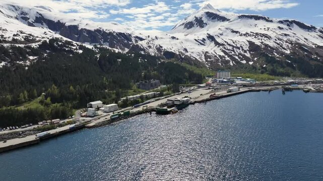 flying across "Passage Canal", along Alaskan mountain Landscape in front of Whittier harbor and port area with Cityscape of Whittier and snow covered mountains in background. 4k aerial video footage 