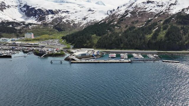 Whittier, Alaska, flying along coastline of Whittier from "Phillips Cruises & Tours" terminal to harbor and port area with Cityscape and mountains in background . 4k aerial video footage
