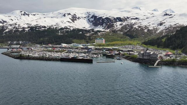 flying along Alaska mountain Landscape in front of Whittier harbor and port area with Cityscape of Whittier and snow covered mountains in background. 4k aerial video footage