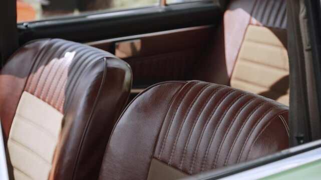 Vintage leather interior of retro car with front seats and back sofa. Interior of comfortable car with open windows on sunny day.