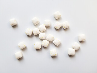 Small white square candies scattered on a plain surface, creating a simple yet inviting display of...
