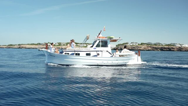 A group of people enjoys a calm summer ride on a classic llaut boat cruising near the coast of Majorca. Summer, vacation, boat concept

