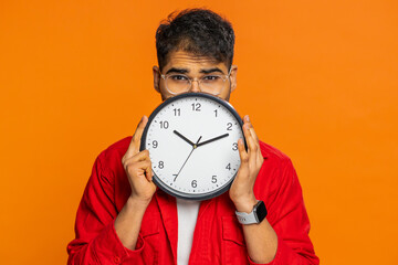 Serious strict Indian man holding office clock hiding behind, checking time on watch, running late...