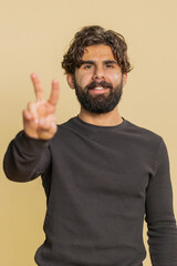 Young Indian man showing victory sign, hoping for success and win, doing peace gesture, smiling...
