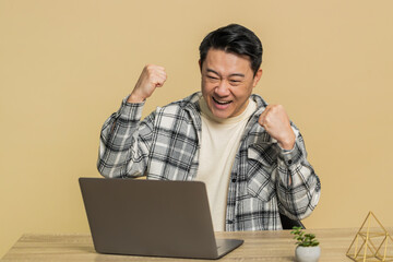 Happy Asian Chinese middle-aged man working on laptop netbook shocked by sudden victory celebrate...