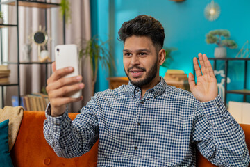 Happy Indian Arabian man blogger taking selfie on smartphone, communicating video call online with...