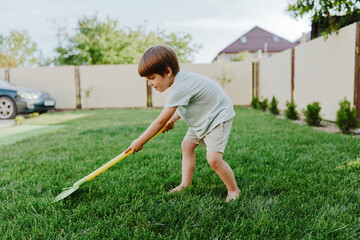 Young boy gardening with a vibrant yellow shovel, enjoying outdoor activity, sunny day, and connecting with nature. Playful and energetic scene in a green lawn.