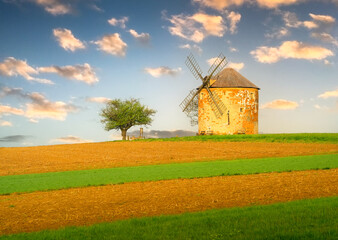 Historic windmill stands tall on a green field under a clear sky at sunset