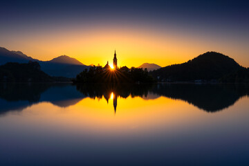 Beautiful sunset over Lake Bled with church silhouette and mountains in the background