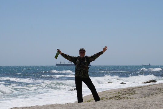 Happy man with raised hands and beer bottle on the beach against the sea horizon