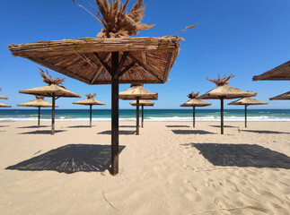 Beach umbrellas covered with straw on an empty sunny sea beach. Beach vacation