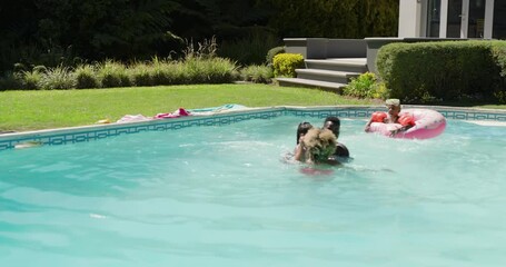 Diverse family grabbing daughter hands from pink tube, lifting floatie-wearing girl in pool for fun - Powered by Adobe