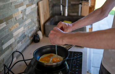 Person cooking scrambled eggs in a frying pan on an induction cooktop, concept of home cooking