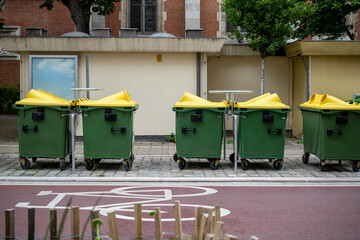 green recycling containers with yellow lids on city street, concept of urban waste segregation