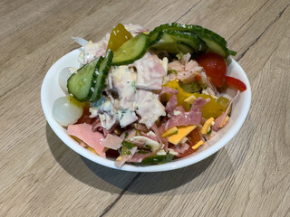 Ham and cheese salad with cucumbers and pickles in white bowl on wooden table