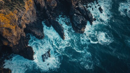 Aerial view of rugged coastline meeting deep ocean waves with rock formations