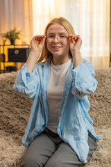 Young woman puts on fashionable glasses frames at home, boosting confidence and clarity for daily...