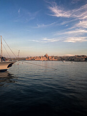 Golden evening light bathes Valletta harbor, where yachts rest peacefully against the backdrop of Malta&rsquo;s historic waterfront and calm sea.