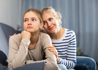 Mother and unhappy teenage daughter sitting after quarrel at home, woman consoles girl