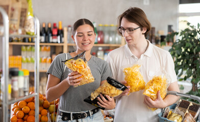 Youth guy with wife choose and buy chips and potato mix crisps in store. Visitors make choice of...