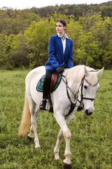 Teenage girl in blue jacket on field with white horse