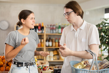 Irritated young man and young woman shoppers quarreling in grocery store