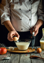 A chef in a white coat cracks an egg into a bowl of milk while surrounded by fresh apples and kitchen tools, showcasing culinary techniques in a warm and inviting setting