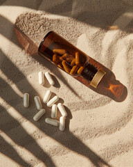 A product photograph of a supplement bottle made of amber glass with a gold cap lying on its side on sand that's a shade of warm beige, with some white capsules spilling out near it.