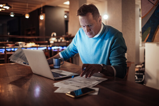 Businessman working from home reviewing documents on his laptop at night