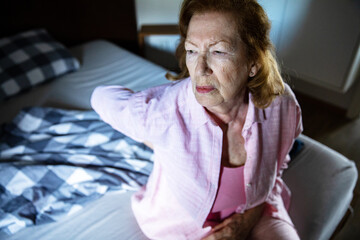 Elderly woman struggling with back pain in bed