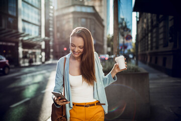 Young woman using a smart phone while walking on a sidewalk in the city