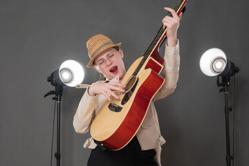 Playful woman guitarist and singer songwriter playing Spanish six string acoustic guitar and sings song with eyes closed, standing on stage. Musician dressed leather jacket and straw hat