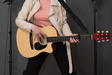 Confidence young female guitarist with Spanish six string acoustic guitar standing full length on stage and looking at camera. Musician dressed in beige leather jacket, straw hat, black jeans pants