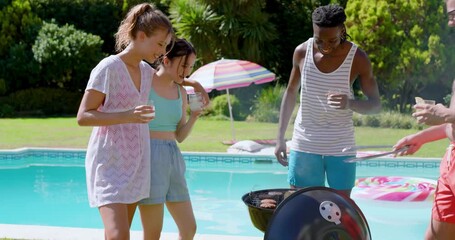 Diverse friends toasting drinks and flipping burgers and corn on charcoal grill for pool barbecue - Powered by Adobe