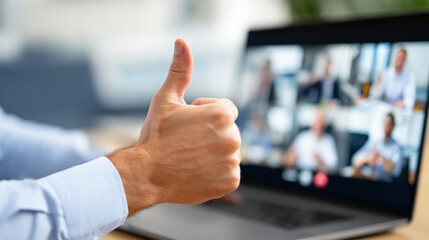 Person giving thumbs up during video conference on laptop screen, showing approval and positivity in professional setting. background is blurred, emphasizing hand gesture and screen