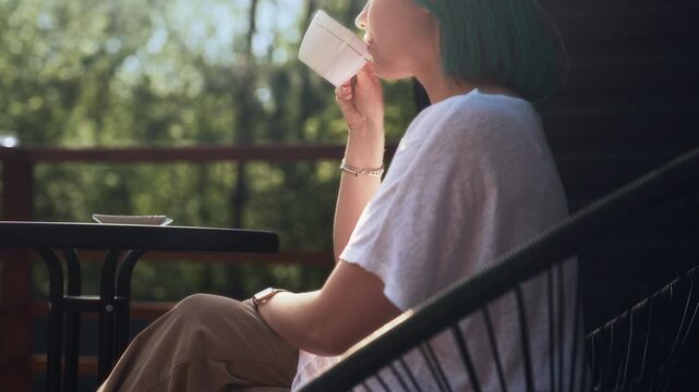Young sipping woman drinks,enjoys morning coffee on terrace of cozy wooden house