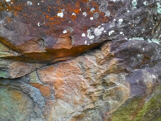 Close-up of a natural rock surface with a rough, uneven texture, visible cracks, and earthy tones,...