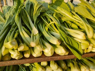 Fresh close-up view of green mustard leaves (Brassica) stacked in a market or kitchen setting,...