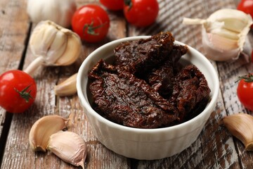 Delicious sun dried tomatoes, fresh vegetables and garlic on wooden table, closeup