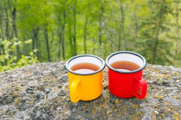 Two metallic tea cups—red, and yellow—on ancient mountain rocks , set against a breathtaking...