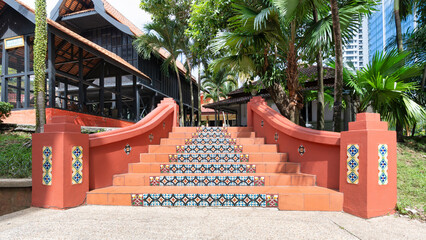 Fototapeta premium Colorful tiled stairs invite visitors to Muzium Negara, showcasing traditional Malaysian architecture. Palm trees and greenery enhance the serene atmosphere, making it a perfect spot for exploration