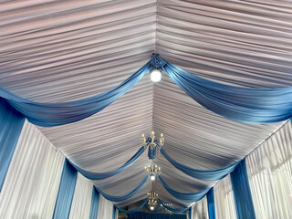Party tent ceiling with wavy white and blue fabric decorated with small round lights