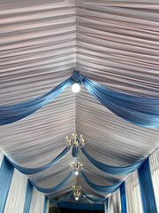 Party tent ceiling with wavy white and blue fabric decorated with small round lights