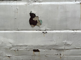 Sheet metal corrosion on an old white car. Corroded surface with a transverse stripe pattern. Damaged and pitted texture. Rusty background. Hole car body detail sheet. Holes in the car body.