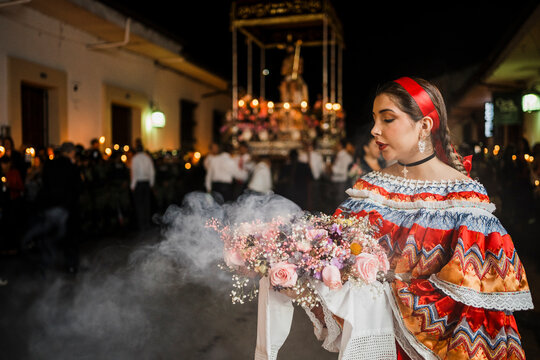 Mujer sahumadora vestida con traje t&iacute;pico tradicional participa en una procesi&oacute;n nocturna durante la Semana Santa en Popay&aacute;n, Colombia. Sostiene un ramo de flores mientras esparce sahumerio 