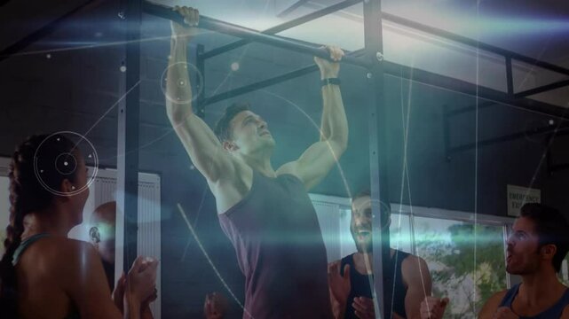 Mid adult man gripping pull-up bar, pulling up in gym, overlaying fitness metrics as group claps