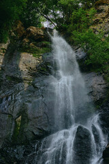 Fototapeta premium waterfall cascading down dark rock cliffs surrounded by lush green trees in a natural outdoor setting with fresh flowing water and vibrant foliage