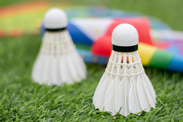 White cream shuttlecock, badminton sport equipment, places on green grass in front of American national flag and rainbow flag, concept for badminton sport for all genders and lgbtq+ people.